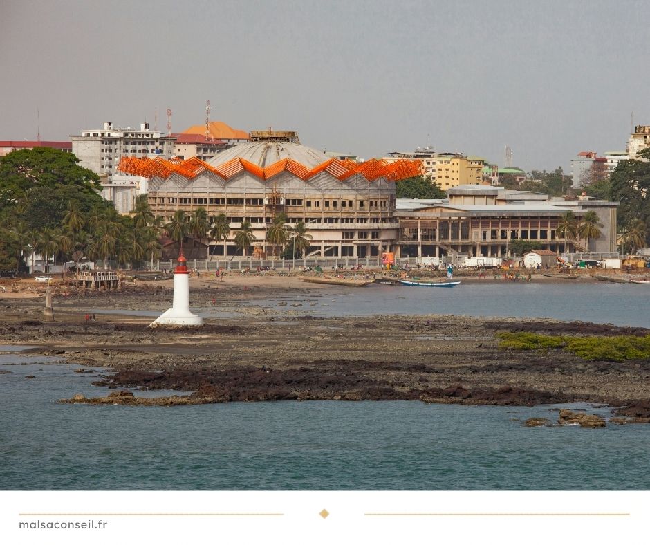Vue côtière de Conakry avec le Palais du Peuple, un phare blanc et la ligne d'horizon de la ville